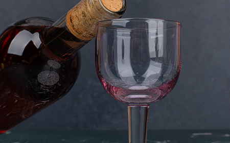 Наливание красного вина из бутылки с пробкой в бокал на тёмном фоне